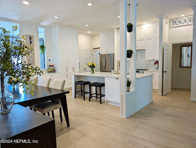 kitchen featuring white cabinetry, a kitchen island with sink, light hardwood / wood-style flooring, stainless steel refrigerator, and a breakfast bar