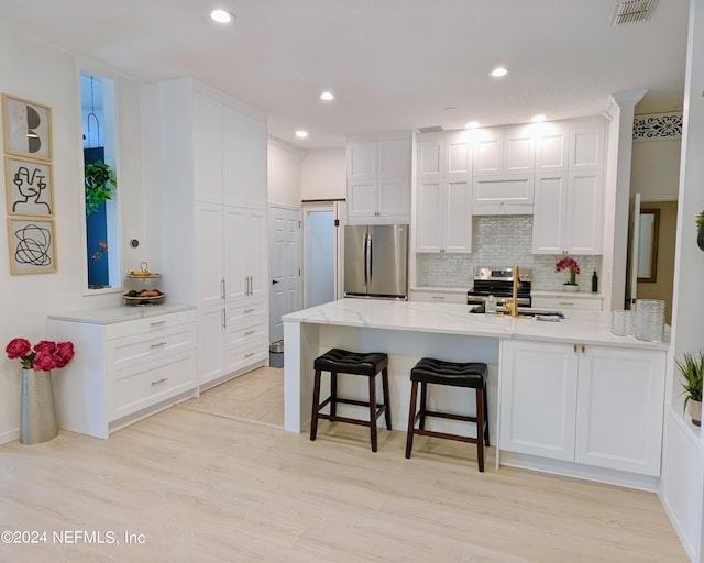 kitchen featuring appliances with stainless steel finishes, a kitchen bar, white cabinets, light hardwood / wood-style flooring, and sink