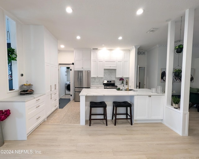 kitchen featuring a kitchen breakfast bar, stainless steel appliances, sink, white cabinetry, and backsplash