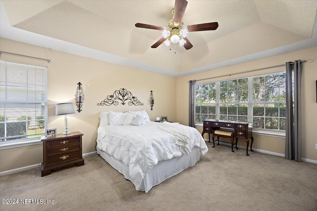 carpeted bedroom featuring multiple windows, ceiling fan, and a tray ceiling