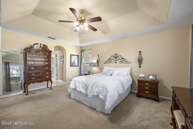 carpeted bedroom with ceiling fan and a raised ceiling