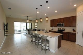 kitchen featuring hanging light fixtures, an island with sink, stainless steel appliances, a kitchen bar, and sink