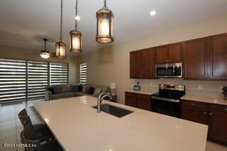 kitchen featuring pendant lighting, sink, a kitchen island with sink, appliances with stainless steel finishes, and a kitchen bar