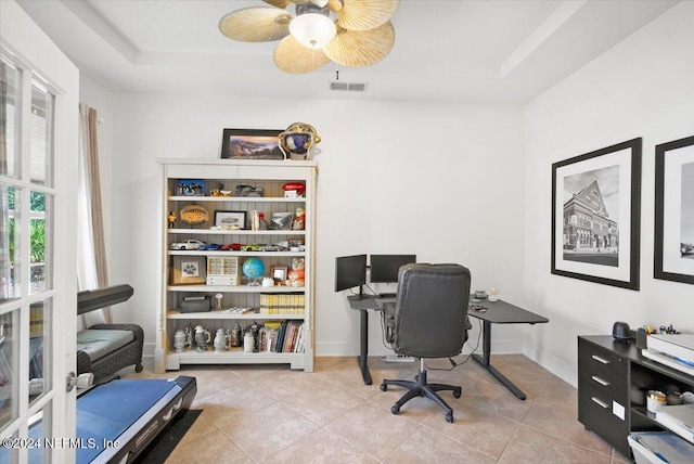 office area featuring a tray ceiling, light tile patterned floors, and ceiling fan