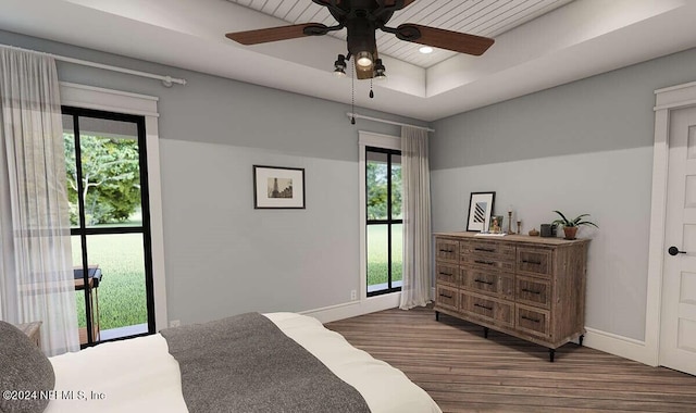 bedroom with ceiling fan, a tray ceiling, dark hardwood / wood-style floors, and multiple windows