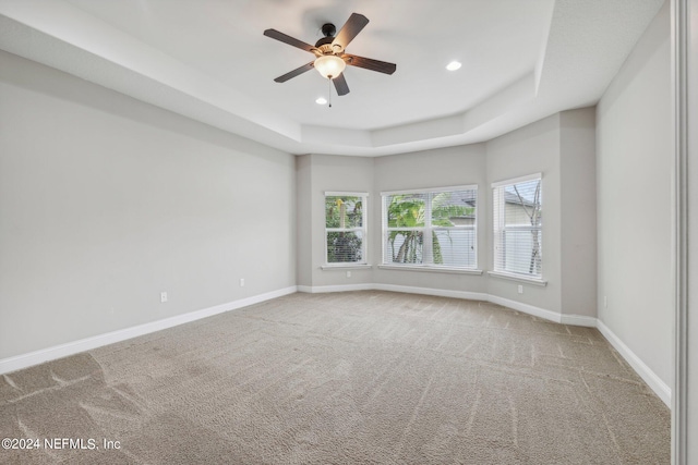 carpeted empty room featuring ceiling fan and a raised ceiling