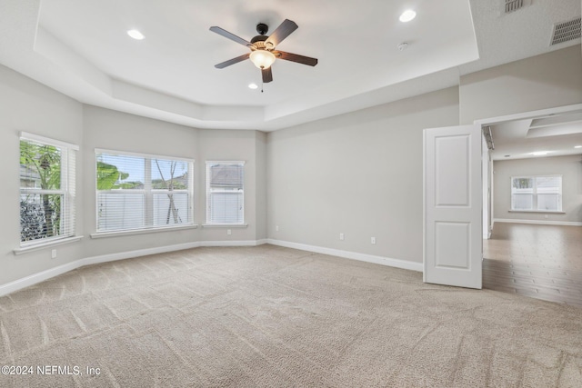 spare room featuring a tray ceiling, ceiling fan, and light colored carpet