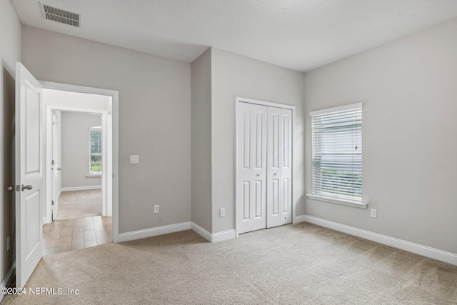 unfurnished bedroom with light carpet, a closet, and a textured ceiling