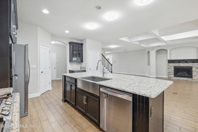 kitchen featuring light wood-type flooring, a center island with sink, appliances with stainless steel finishes, and a stone fireplace