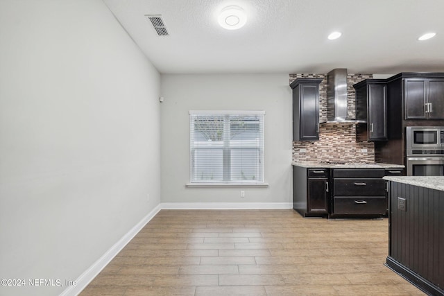 kitchen with decorative backsplash, stainless steel appliances, light hardwood / wood-style floors, and wall chimney range hood