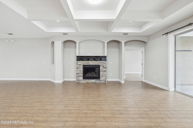 unfurnished living room with a stone fireplace, coffered ceiling, light hardwood / wood-style flooring, and beamed ceiling