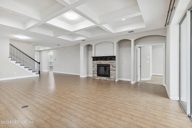 unfurnished living room featuring light hardwood / wood-style flooring, beamed ceiling, coffered ceiling, and a stone fireplace