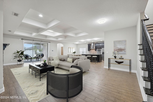 living room with light wood-type flooring, beam ceiling, a textured ceiling, and coffered ceiling