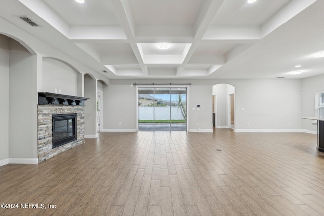 unfurnished living room featuring a stone fireplace, coffered ceiling, hardwood / wood-style floors, and beamed ceiling