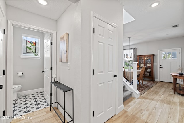 hall with an inviting chandelier, light hardwood / wood-style flooring, and a textured ceiling