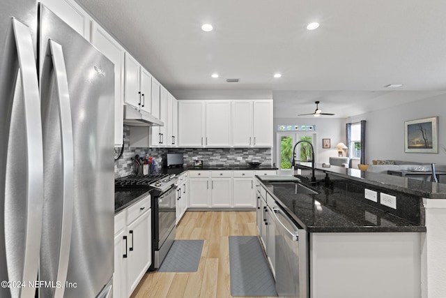 kitchen featuring appliances with stainless steel finishes, white cabinetry, sink, dark stone countertops, and a center island with sink