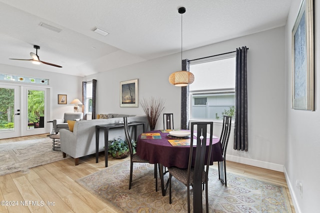 dining space with ceiling fan, a textured ceiling, light hardwood / wood-style floors, and french doors