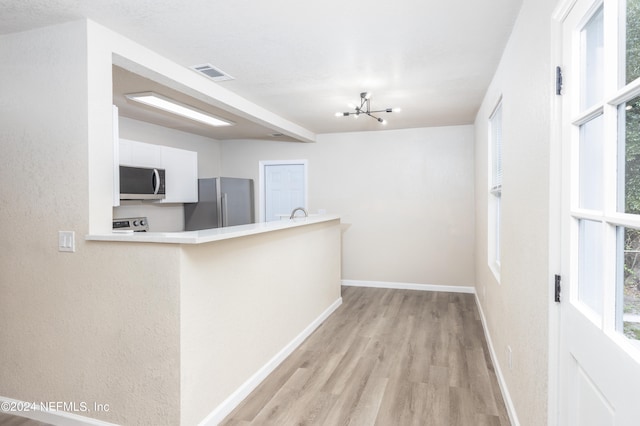 kitchen featuring appliances with stainless steel finishes, a healthy amount of sunlight, a notable chandelier, and white cabinets