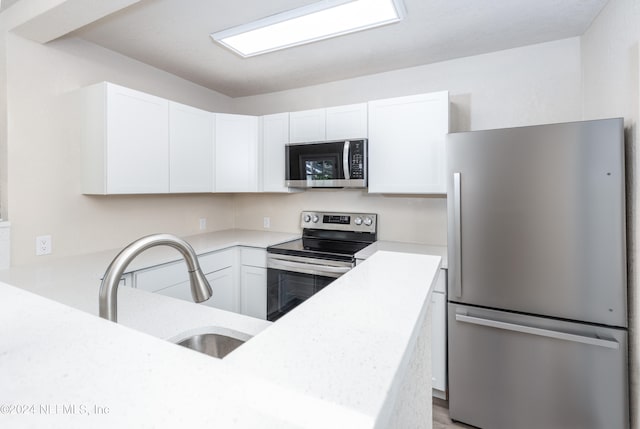 kitchen featuring sink, white cabinets, kitchen peninsula, appliances with stainless steel finishes, and light stone countertops