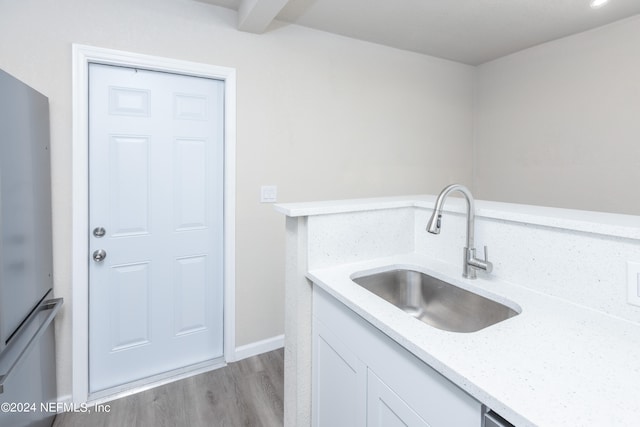 kitchen with light stone counters, white cabinets, fridge, light hardwood / wood-style flooring, and sink