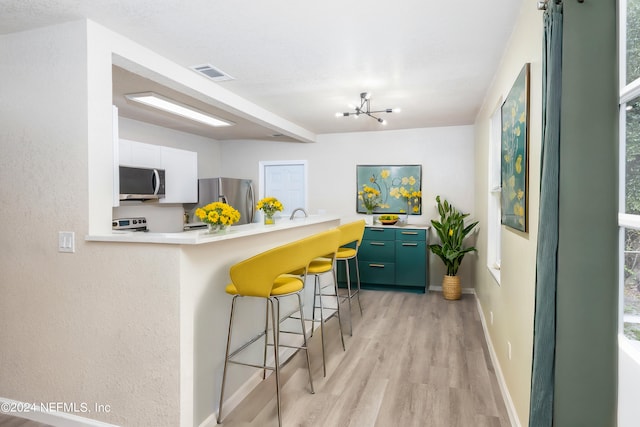 kitchen with light hardwood / wood-style flooring, white cabinetry, stainless steel appliances, green cabinets, and a kitchen bar