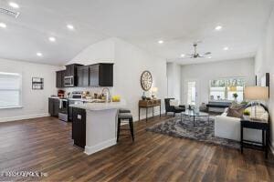 kitchen featuring dark wood-type flooring, dark brown cabinetry, lofted ceiling, a breakfast bar, and appliances with stainless steel finishes