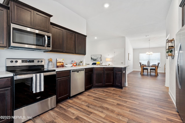 kitchen featuring pendant lighting, wood-type flooring, dark brown cabinets, kitchen peninsula, and stainless steel appliances