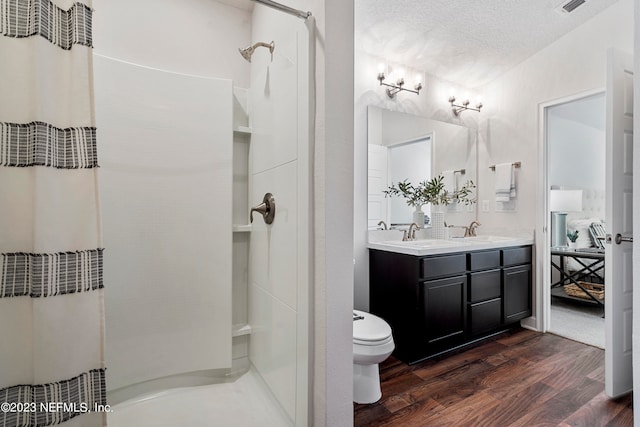 bathroom featuring wood-type flooring, a textured ceiling, a shower with shower curtain, vanity, and toilet