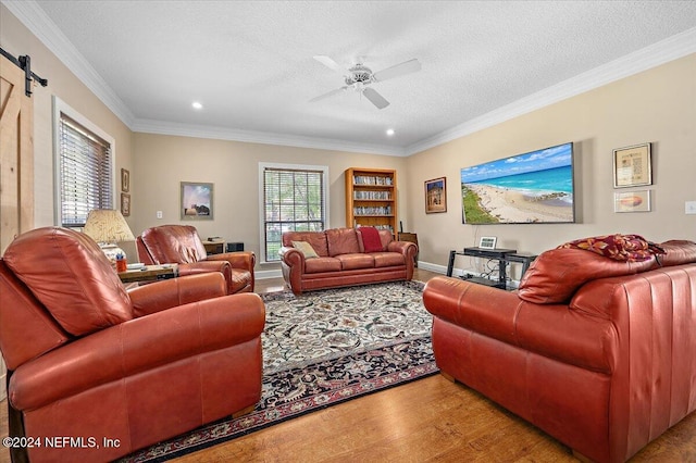 living room with ceiling fan, light hardwood / wood-style floors, a barn door, ornamental molding, and a textured ceiling