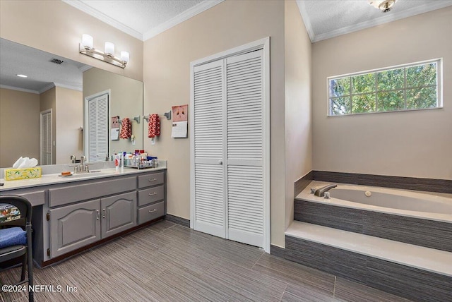 bathroom featuring a relaxing tiled tub, vanity, crown molding, and a textured ceiling