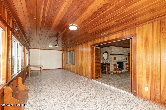 interior space featuring wooden walls, ceiling fan, a fireplace, and wooden ceiling