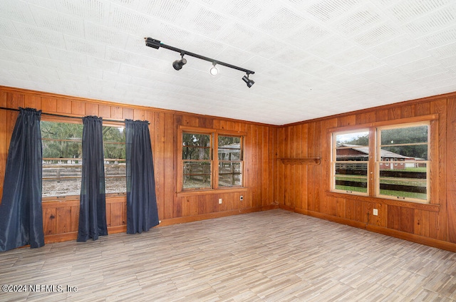 empty room with wooden walls, light wood-type flooring, and rail lighting