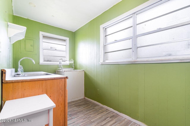 clothes washing area featuring wooden walls, sink, and light hardwood / wood-style flooring