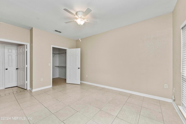 unfurnished bedroom featuring ceiling fan, a closet, light tile patterned floors, and a walk in closet