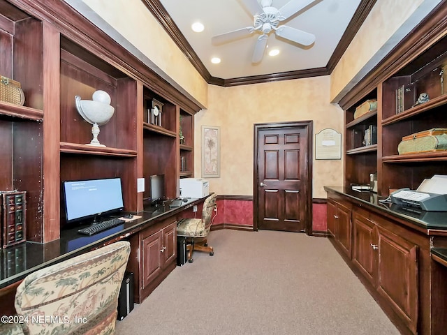 home office featuring carpet flooring, baseboards, built in desk, a ceiling fan, and crown molding