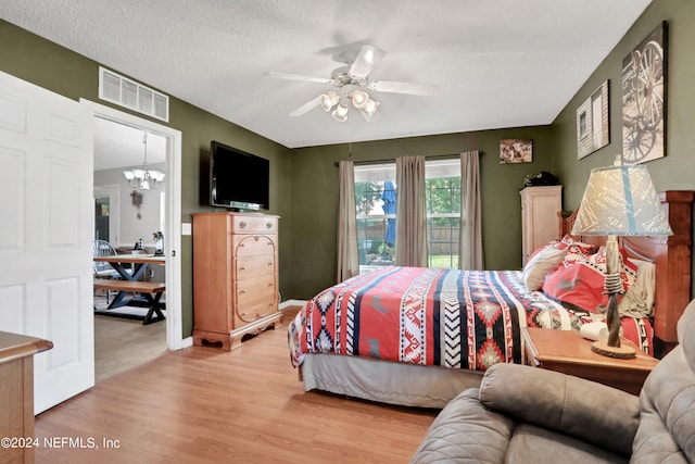 bedroom with hardwood / wood-style flooring, ceiling fan with notable chandelier, and a textured ceiling