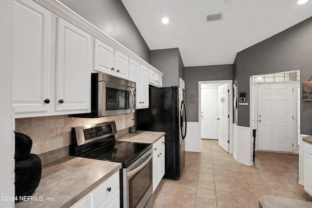 kitchen featuring light tile patterned flooring, white cabinets, vaulted ceiling, stainless steel appliances, and backsplash