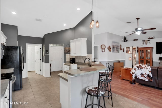 kitchen featuring lofted ceiling, kitchen peninsula, white cabinetry, a kitchen breakfast bar, and stainless steel electric range oven