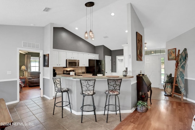 kitchen with white cabinets, appliances with stainless steel finishes, kitchen peninsula, and a breakfast bar