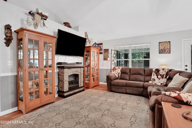 living room with a stone fireplace, light hardwood / wood-style floors, lofted ceiling, and french doors