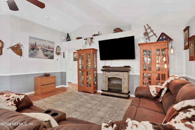 living room with light wood-type flooring, a stone fireplace, vaulted ceiling, and ceiling fan