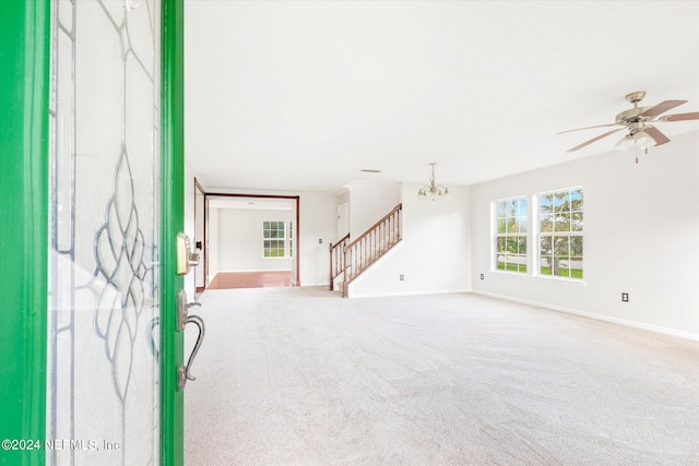 unfurnished living room featuring ceiling fan with notable chandelier and light carpet