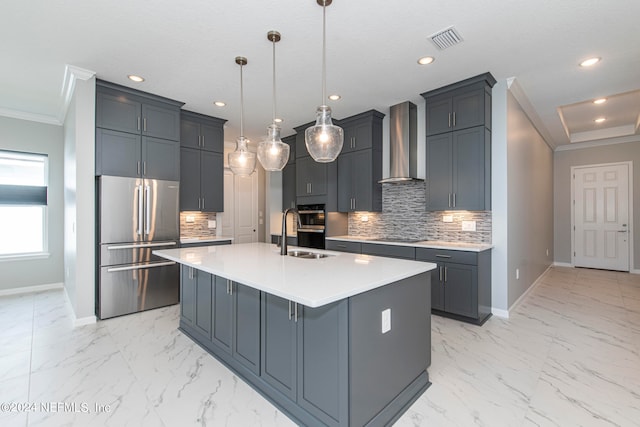 kitchen featuring wall chimney exhaust hood, a kitchen island with sink, crown molding, decorative light fixtures, and stainless steel fridge