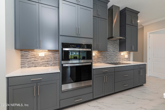 kitchen featuring stainless steel double oven, ornamental molding, wall chimney range hood, gray cabinets, and decorative backsplash