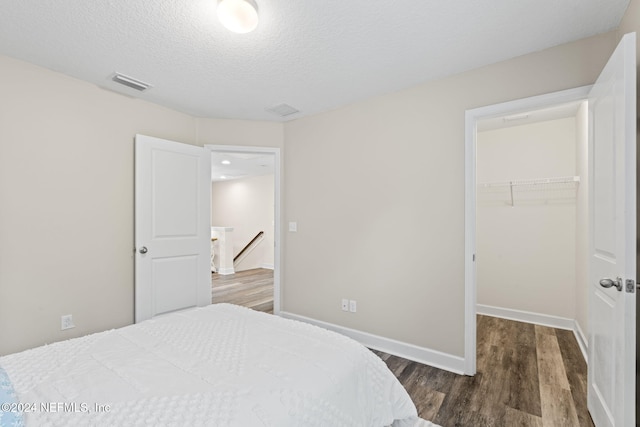 bedroom with a textured ceiling, a walk in closet, a closet, and dark hardwood / wood-style flooring