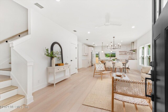 living room with ceiling fan with notable chandelier and light hardwood / wood-style floors