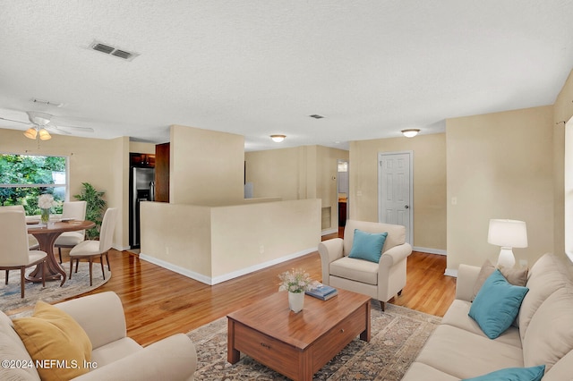 living room with a textured ceiling, light hardwood / wood-style floors, and ceiling fan