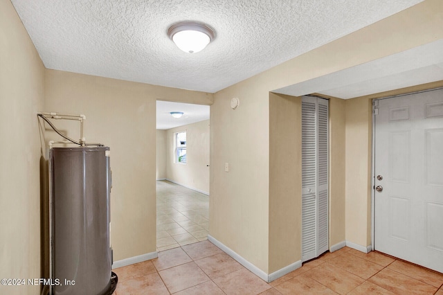 corridor with water heater, a textured ceiling, and light tile patterned floors