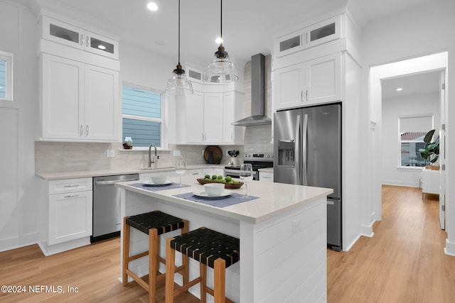 kitchen featuring appliances with stainless steel finishes, white cabinetry, tasteful backsplash, wall chimney exhaust hood, and decorative light fixtures