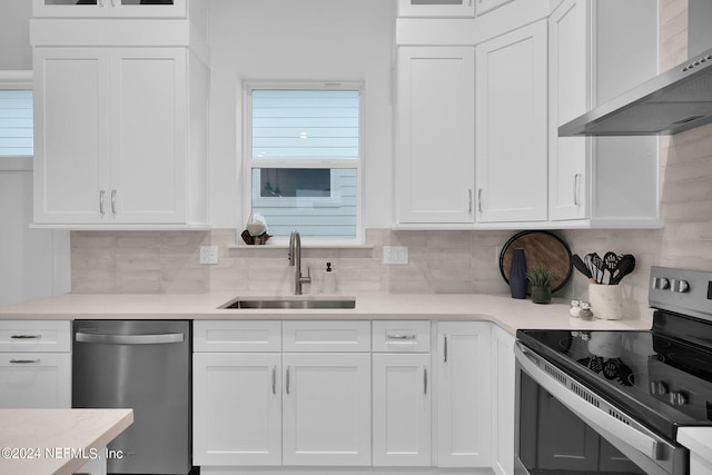 kitchen with appliances with stainless steel finishes, white cabinetry, backsplash, sink, and wall chimney range hood